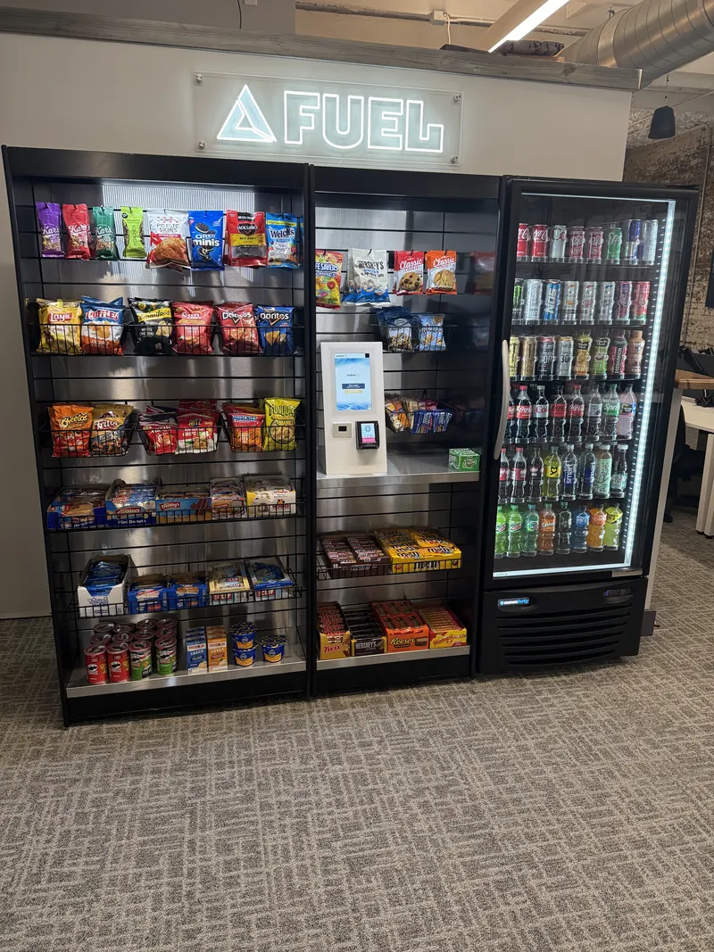 A self-checkout micro market with snack racks, a pay kiosk, and a drink cooler